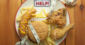 Photo of a heap of junk food on a set of scales saying "HELP". A tape measure is entwined around the junk food.